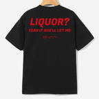 A black short-sleeve t-shirt hanging on a wooden hanger against a light gray background, featuring bold red text on the back that reads 'LIQUOR? YEAH IF SHE'LL LET ME' with a small red graphic below.