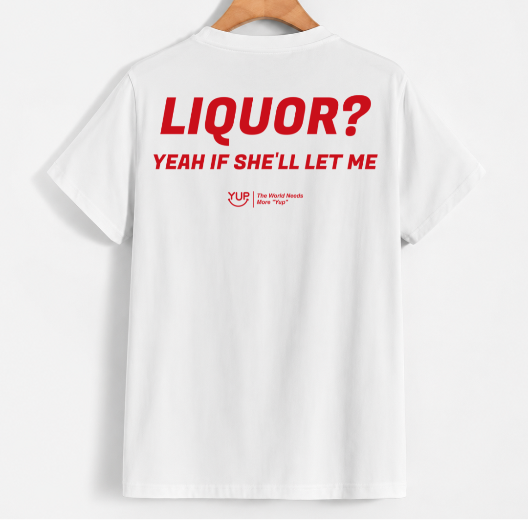 White short-sleeve t-shirt hanging on a wooden hanger, showing the back with bold red text that reads 'LIQUOR? YEAH IF SHE'LL LET ME' and a small red YUP logo underneath.