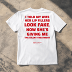 A white short-sleeve t-shirt with bold red text on the front reading 'I TOLD MY WIFE HER LIP FILLERS LOOK FAKE. NOW SHE'S GIVING ME THE SILENT TREATMENT'.