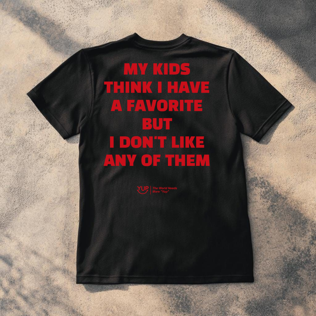 A black short-sleeve t-shirt laid flat on a textured concrete surface with dappled shadows. The back of the shirt features bold red text that reads 'HAS ANYONE EVER BEEN BORN FROM A MAN?' with a small red 'YUP' logo underneath.