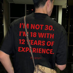 A man viewed from behind wearing a black t-shirt with bold red text that reads 'I'M NOT 30. I'M 18 WITH 12 YEARS OF EXPERIENCE.
