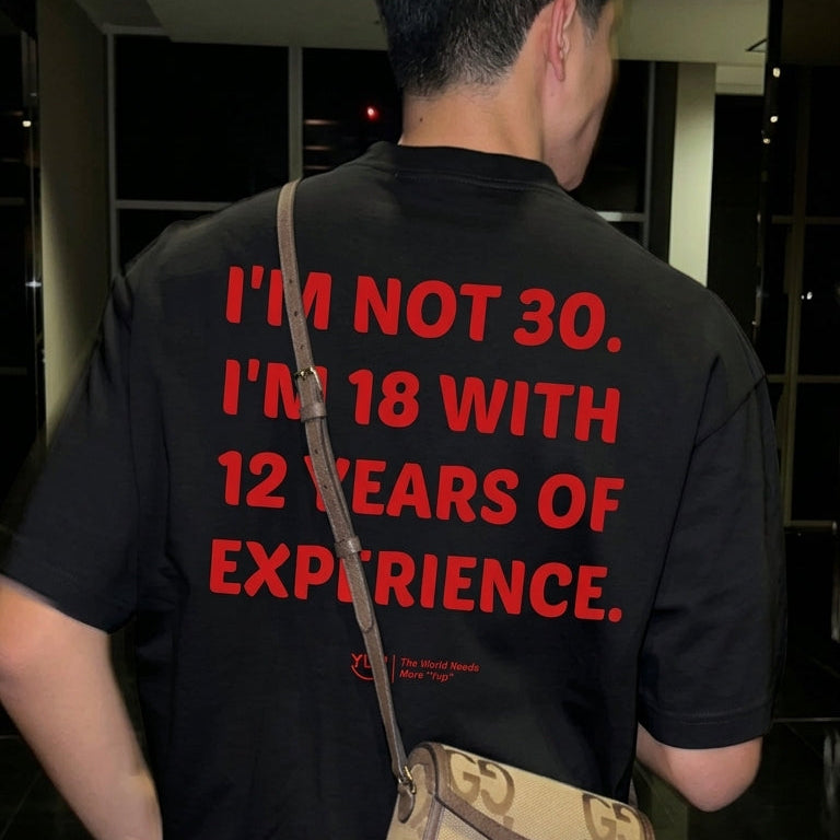 A man viewed from behind wearing a black t-shirt with bold red text that reads 'I'M NOT 30. I'M 18 WITH 12 YEARS OF EXPERIENCE.
