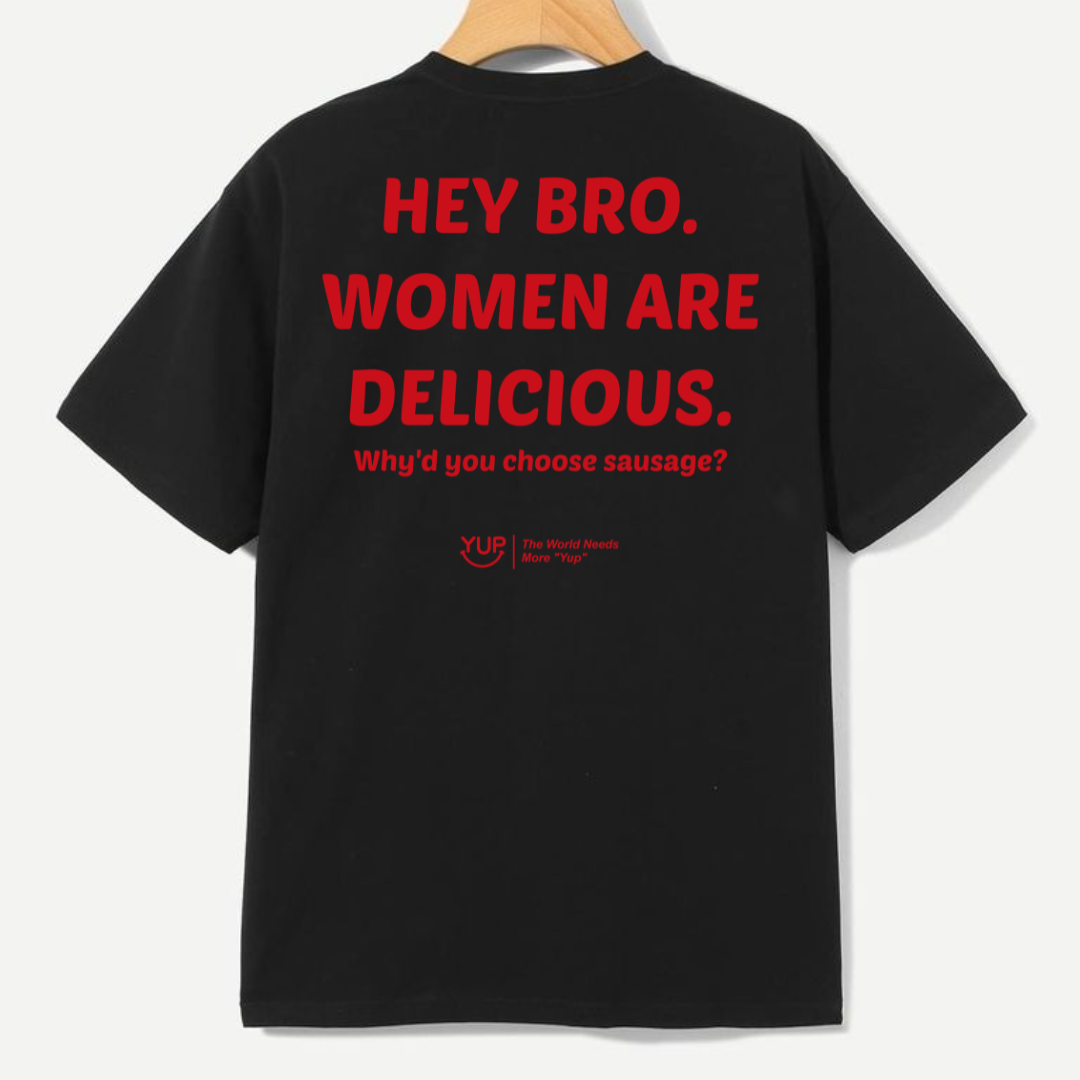 A black short-sleeve t-shirt hanging on a wooden hanger, showing the back with bold red text that reads 'HEY BRO. WOMEN ARE DELICIOUS.