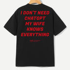 A black short-sleeve t-shirt hanging on a wooden hanger against a light gray background, featuring a bold red text graphic on the back that reads 'I DON'T NEED CHATGPT MY WIFE KNOWS EVERYTHING' with a small red 'Yupoong' logo underneath.