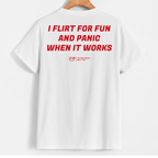 White short-sleeve t-shirt hanging on a wooden hanger, showing the back with bold red text that reads 'I FLIRT FOR FUN AND PANIC WHEN IT WORKS' and a small red 'YUS' logo underneath.