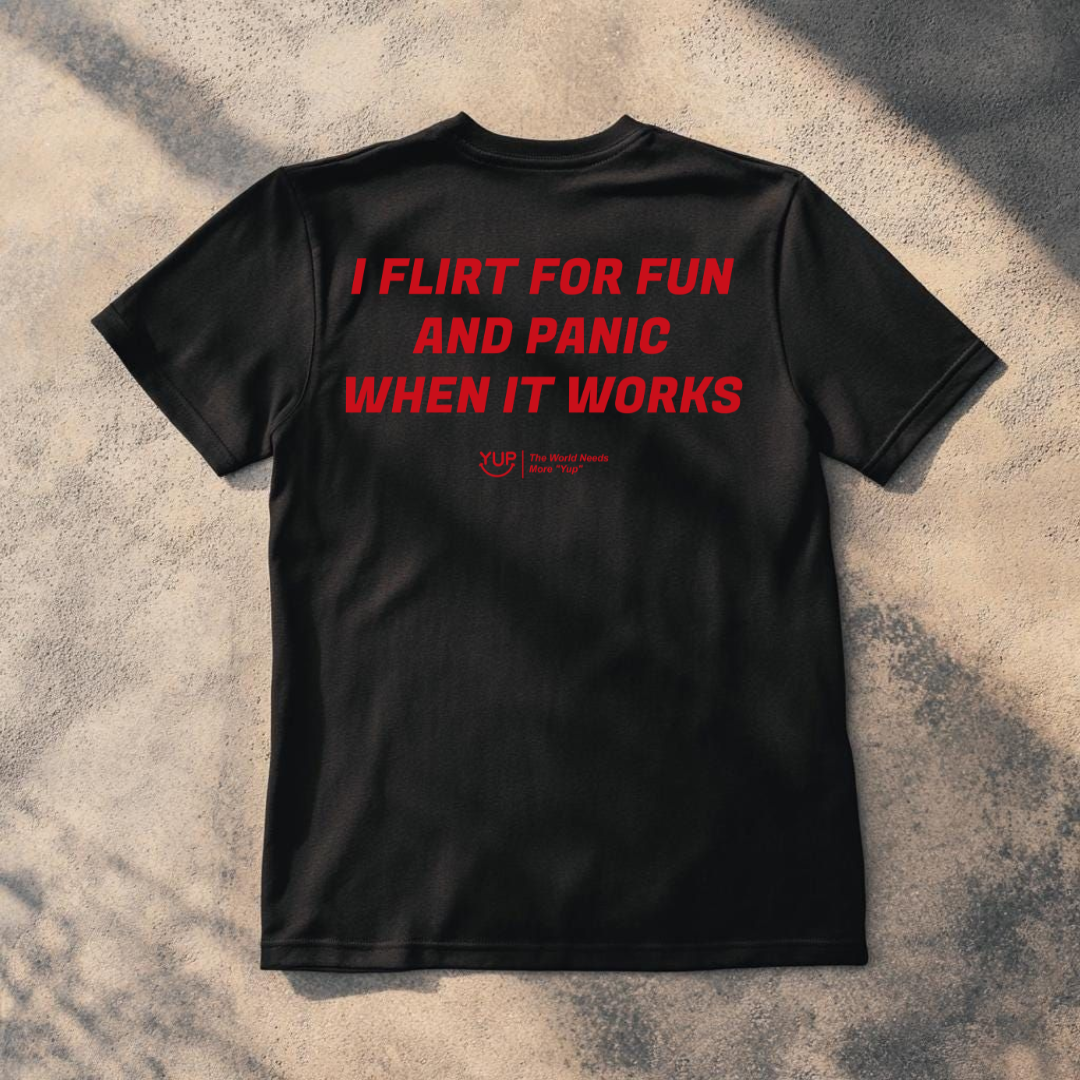 A black short-sleeve t-shirt laid flat on a textured concrete surface with dappled shadows. The back of the shirt features the phrase 'When you Excel They will spreadsheet about you' printed in a bold red font.