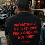 A man seen from behind wearing a black t-shirt with bold red text that reads 'CREMATION IS MY LAST HOPE FOR A SMOKING HOT BODY' on a wooden deck at an outdoor bar.