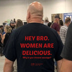 A man viewed from behind wearing a black t-shirt with bold red text that reads 'HEY BRO. WOMEN ARE DELICIOUS.
