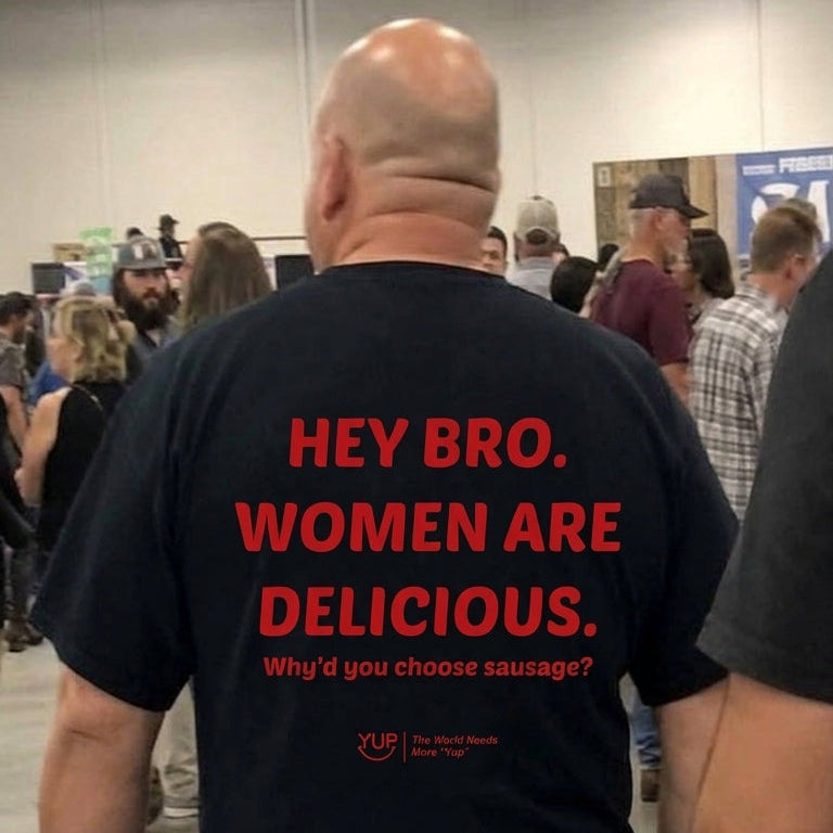 A man viewed from behind wearing a black t-shirt with bold red text that reads 'HEY BRO. WOMEN ARE DELICIOUS.