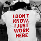 A person sitting at a desk with their head resting on a laptop, wearing a white t-shirt with bold red text on the back that reads 'I DON'T KNOW. I JUST WORK HERE'.
