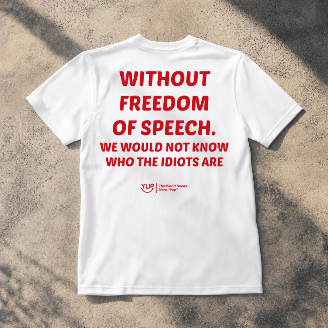A white short-sleeve T-shirt laid flat on a textured concrete surface with dappled shadows. The shirt has large red text reading 'WITHOUT FREEDOM OF SPEECH.