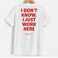 White short-sleeve T-shirt hanging on a wooden hanger, shown from the back with large red text reading 'I DON'T KNOW. I JUST WORK HERE' and a small red 'Yup' logo near the lower back.