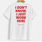 White short-sleeve T-shirt hanging on a wooden hanger, shown from the back with large red text reading 'I DON'T KNOW. I JUST WORK HERE' and a small red 'Yup' logo near the lower back.