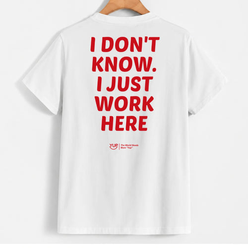 White short-sleeve T-shirt hanging on a wooden hanger, shown from the back with large red text reading 'I DON'T KNOW. I JUST WORK HERE' and a small red 'Yup' logo near the lower back.