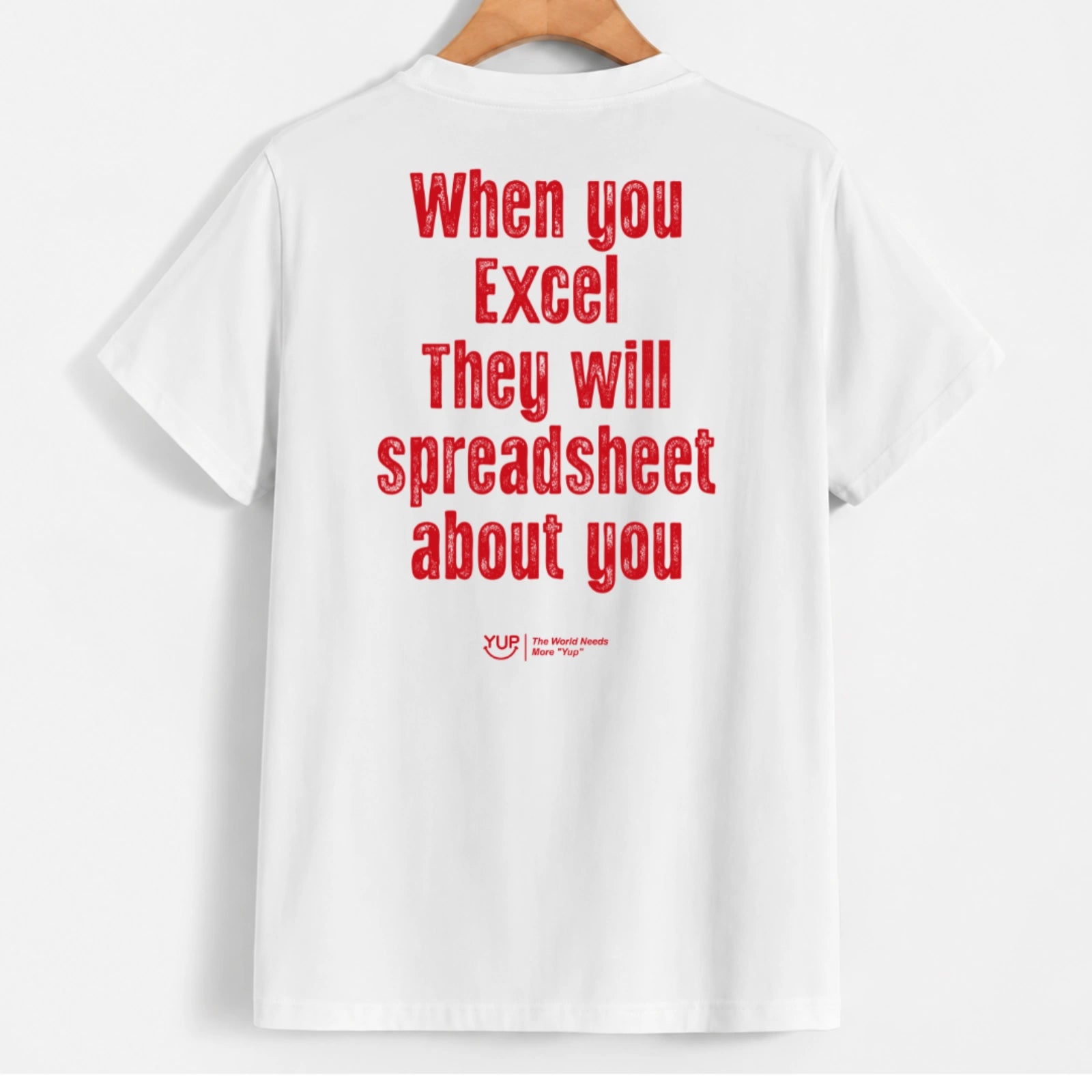 White short-sleeve t-shirt hanging on a wooden hanger, featuring a humorous red text graphic on the back that reads 'When you Excel They will spreadsheet about you' with a small 'XLF The Excel Fan Club' logo below.